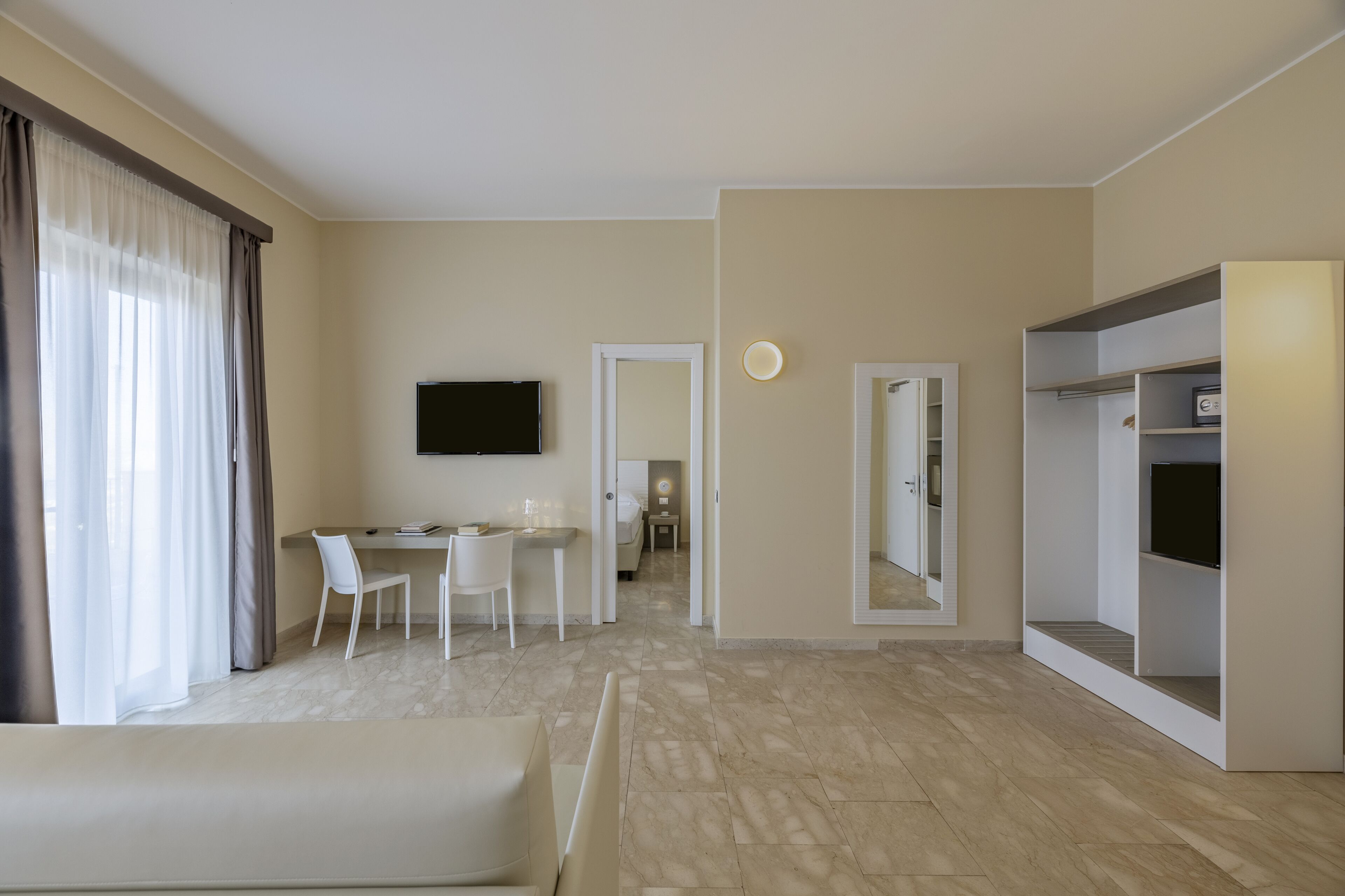 Une chambre d’hôtel moderne dotée d’une télévision à écran plat, d’un coin repas avec une table et des chaises, d’un grand miroir et d’une armoire.