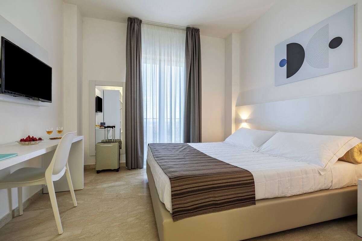 Una habitación de hotel con una cama, un escritorio, una silla, un televisor y una obra de arte en la pared.
