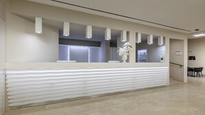 A reception area with a modern design, featuring a reception desk, a vase with flowers, and a staircase in the background. - Venere di Erice Resort (Valderice)