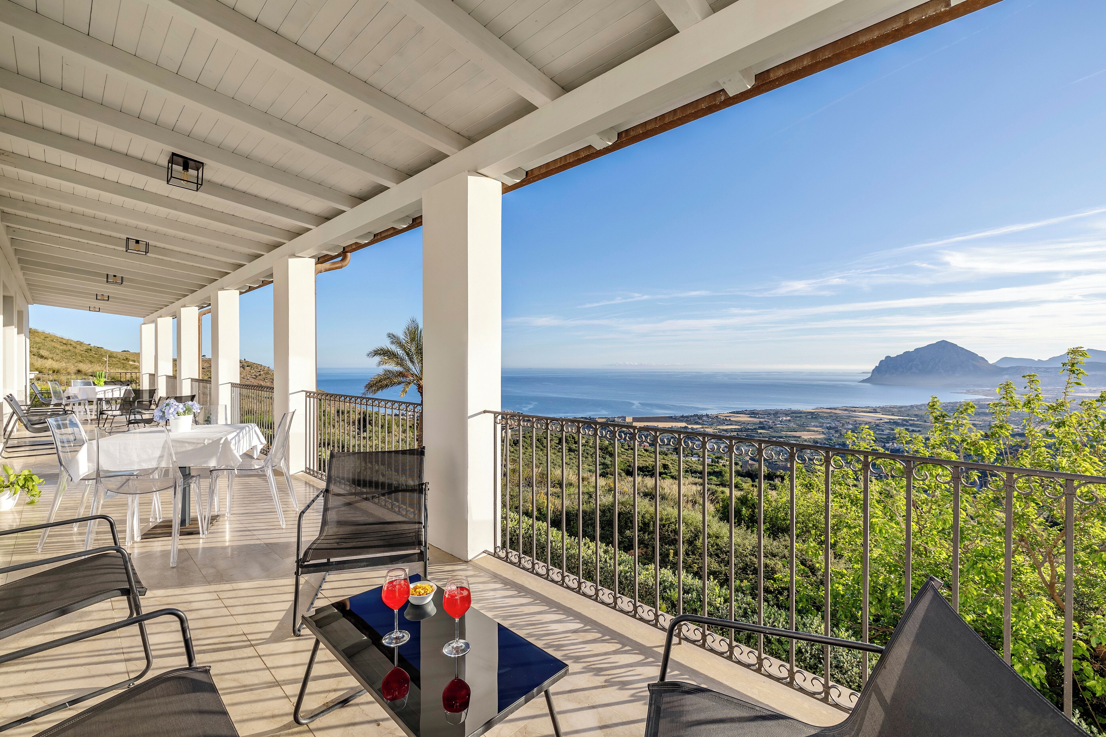 A covered outdoor dining area with a table set for two, overlooking a scenic view of the ocean and hills.