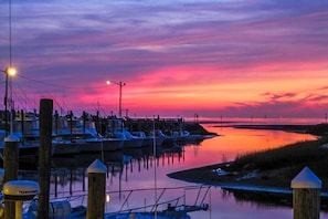 Um pôr do sol sobre um porto com barcos atracados, um cais e águas calmas refletindo o céu.