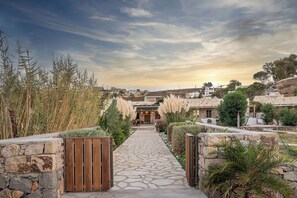 A stone pathway leading to a building with a wooden gate, surrounded by greenery and stone walls. - Beachfront Villa with private mini pool / jacuzzi (Patmos)