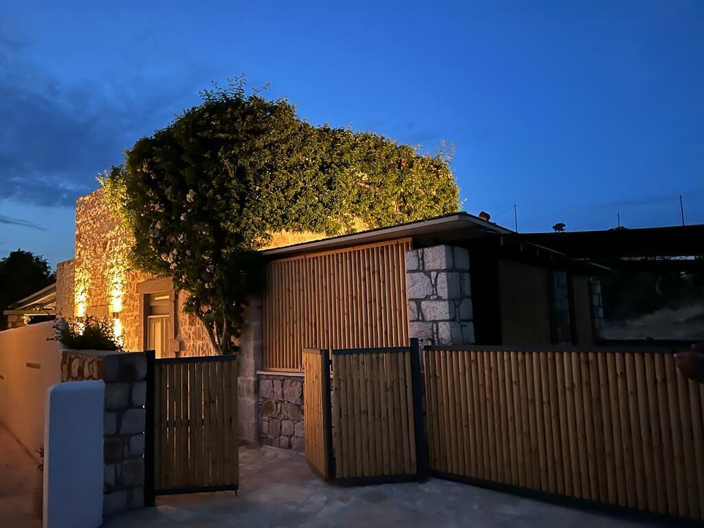 Edifici de pedra amb una tanca de fusta i un teulat cobert de vegetació.