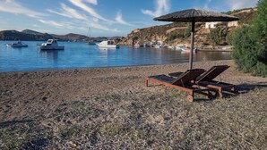 Una spiaggia con lettini e un ombrellone, barche in acqua e un edificio sullo sfondo.