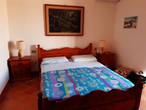 Ein ordentlich bezogenes Bett mit einer farbenfrohen Decke, zwei Nachttische mit Lampen, ein gerahmtes Bild an der Wand und ein kleines Gemälde an der Wand.