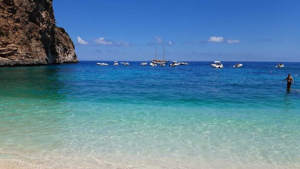 Ein Strand mit klarem türkisblauem Wasser, Booten und einer felsigen Klippe.