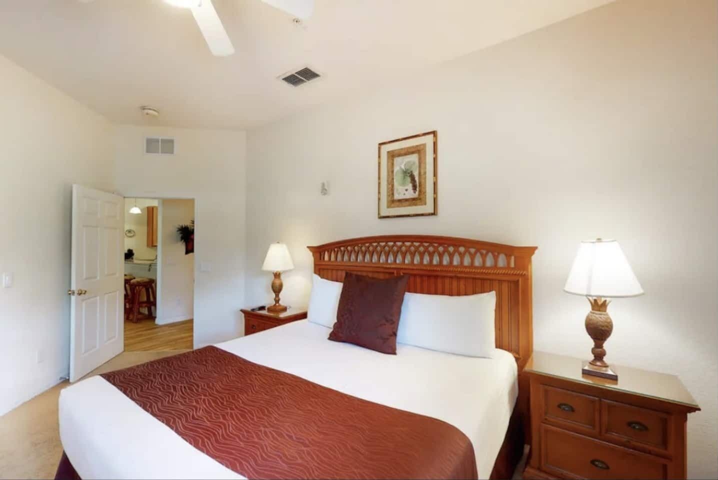 A hotel room with a large bed, two bedside tables with lamps, a wooden headboard, a framed picture on the wall, and a door leading to a bathroom.