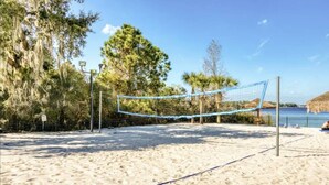 Una cancha de voleibol de playa con red, rodeada de arena y árboles.