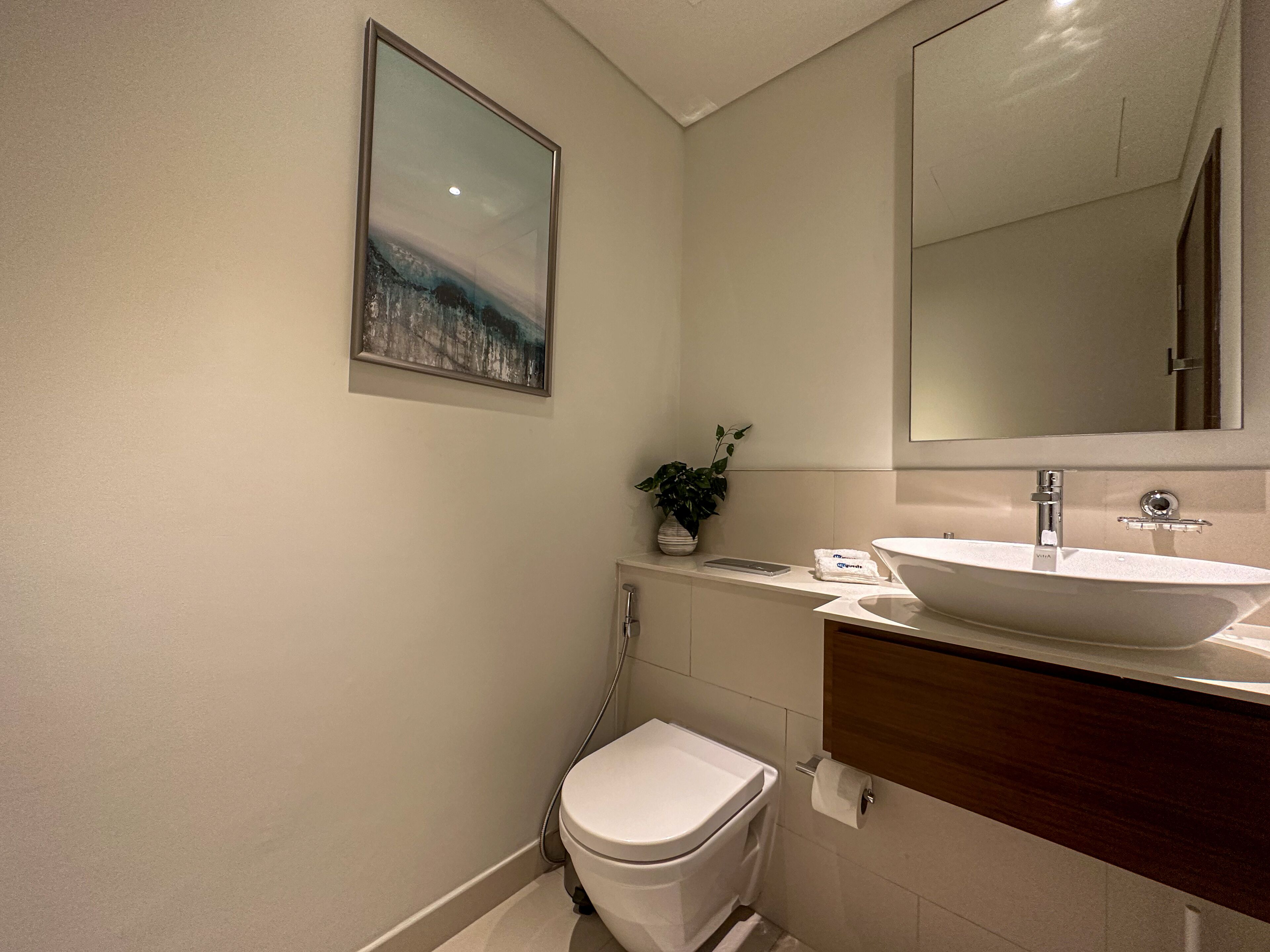 Un baño moderno con inodoro blanco, un espejo grande, un lavamanos y un cuadro en la pared.