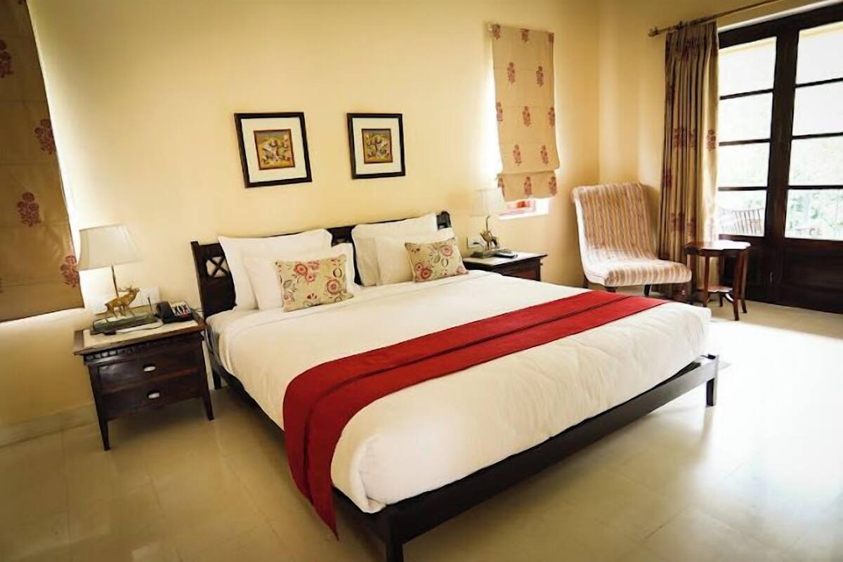 A neatly made bed with a red blanket, a chair, and two bedside tables with lamps.