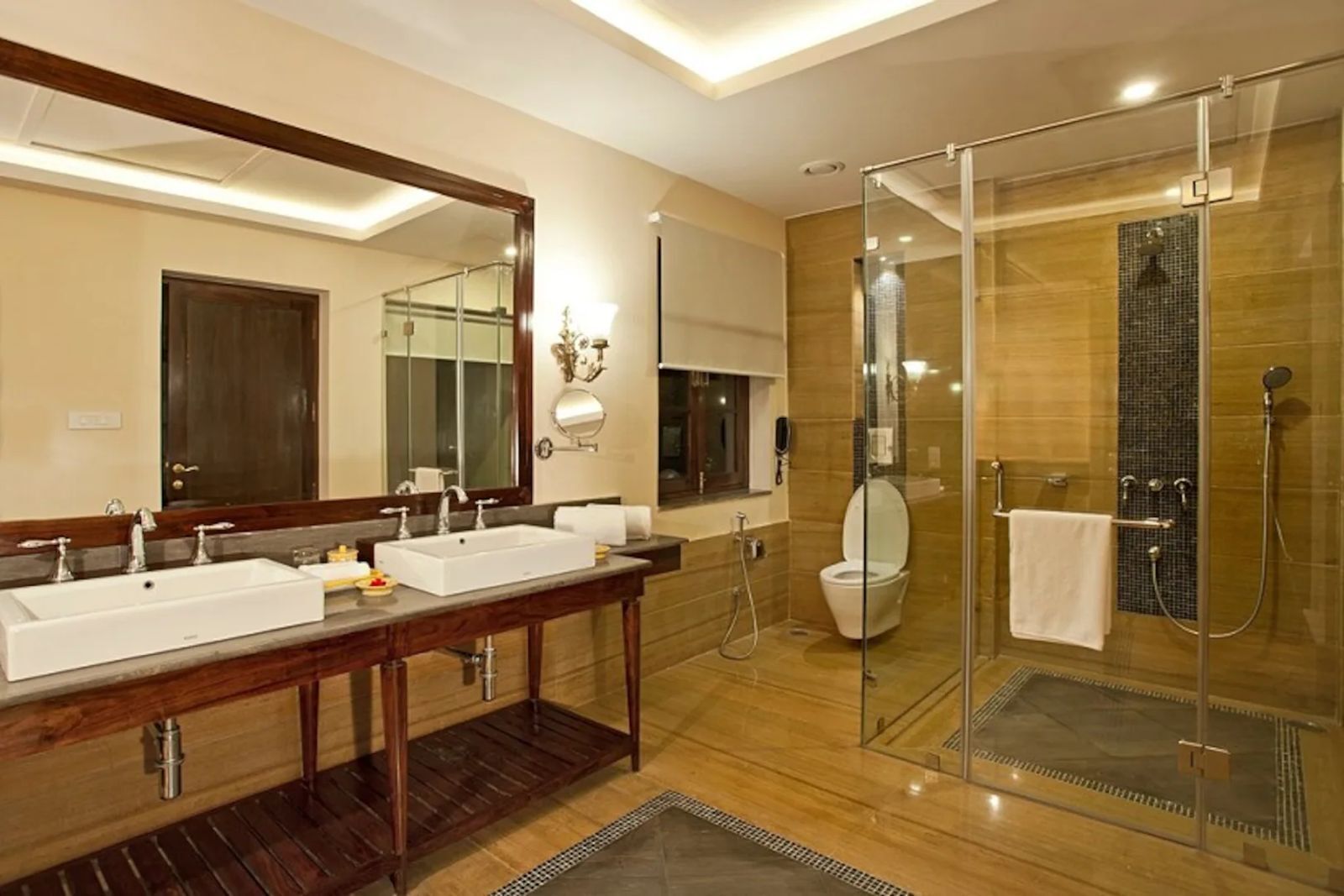 Een moderne badkamer met twee wastafels, een grote spiegel, een douche met glazen wanden en een houten wastafelmeubel.
