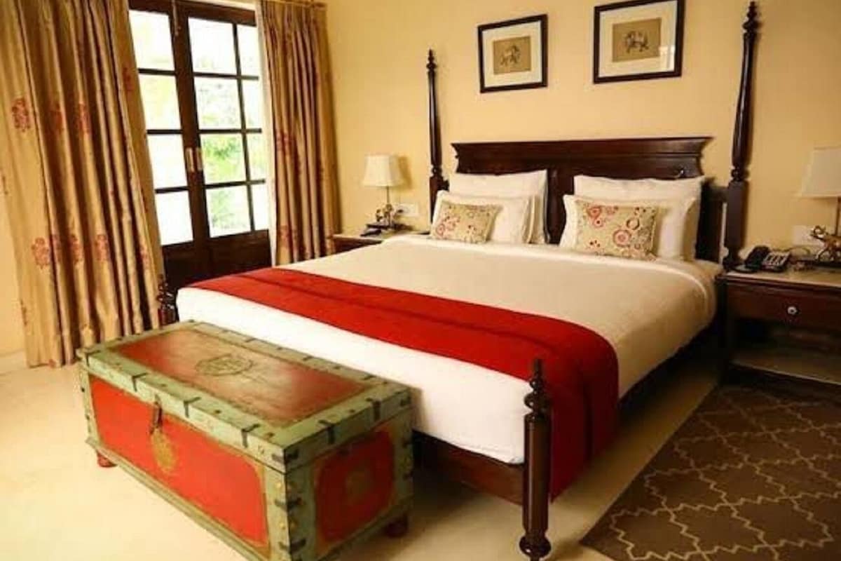 Une chambre d’hôtel avec un grand lit, une tête de lit en bois, deux tableaux encadrés au mur, une table de chevet avec une lampe et une vieille malle servant de table d’appoint.