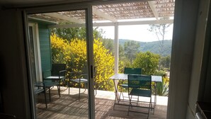 A sliding glass door leading to an outdoor patio with a table and chairs, surrounded by greenery and trees. - Secluded chalet with private access and panoramic views (Draguignan)