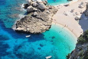 Una zona costera con aguas azules cristalinas, formaciones rocosas y una playa de arena.