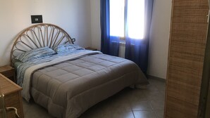 A bedroom with a bed, a nightstand, a wardrobe, and a window with curtains. - Vacation home "The White Myrtle" (Arbatax)
