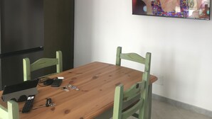 A dining area with a wooden table and green chairs, a black refrigerator, and a TV mounted on the wall. - Vacation home "The White Myrtle" (Arbatax)