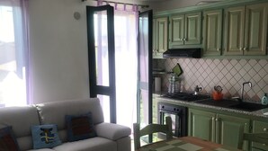 A compact living space with a kitchenette, a dining table, and a sofa with decorative pillows. - Vacation home "The White Myrtle" (Arbatax)