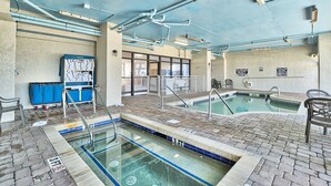 An indoor swimming pool with a tiled floor, a diving board, and a changing room with a blue cart.