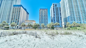 A beachfront hotel with high-rise buildings, palm trees, and a sandy beach.