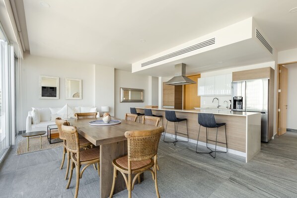 Una cocina moderna con una isla central, un comedor con sillas de mimbre y un sofá con cojines.