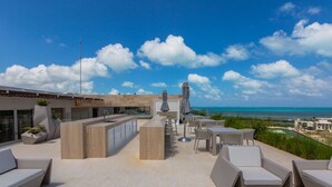 Eine Dachterrasse mit Außenmöbeln, einer Bar und Blick auf den Ozean.