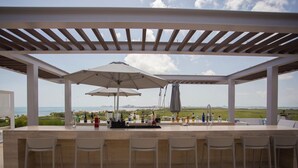 Eine Außenbar mit Meerblick, überdacht mit einer Pergola und Sonnenschirmen.
