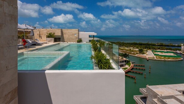 Ein Resort-Pool mit klarem, blauem Wasser, Blick auf den Ozean und eine entfernte Küstenlinie.