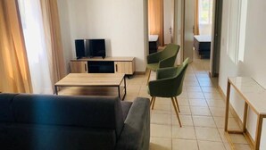A modern living room with a sofa, a TV, a wooden table, and green chairs. - Welcome to Filippi Furnished Bungalows! (PORTO-VECCHIO)