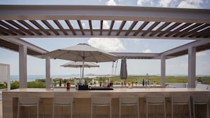 An outdoor bar area with a view of the ocean, covered with a pergola and umbrellas. - Rooftop pool- family apartment- ocean view -close (Cancún)