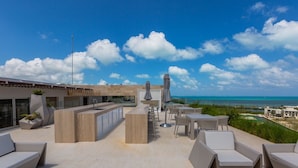 A rooftop terrace with outdoor seating, a bar area, and a view of the ocean. - Rooftop pool- family apartment- ocean view -close (Cancún)