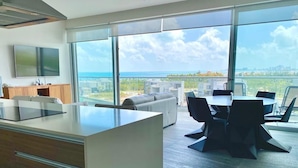 A modern kitchen with a large island, dining area with black chairs, and a large window overlooking the ocean. - Rooftop pool- family apartment- ocean view -close (Cancún)