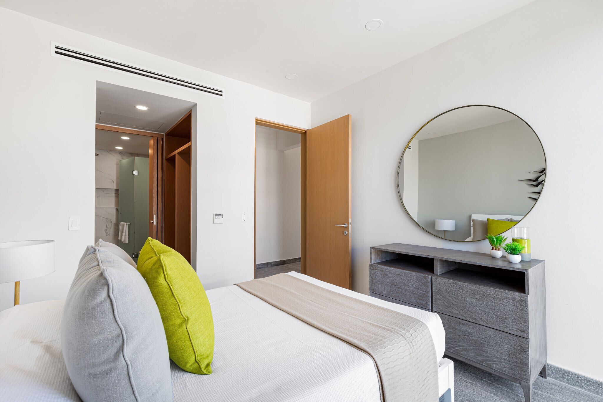 Una habitación de hotel moderna con cama, mesita de noche, espejo y armario.