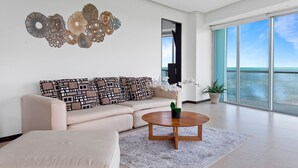 Una sala de estar moderna con un sofá color beige, una mesa redonda de centro y un amplio ventanal con vistas al mar.