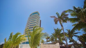 Un hotel alto y moderno con fachada curva, rodeado de palmeras y un cielo azul despejado.