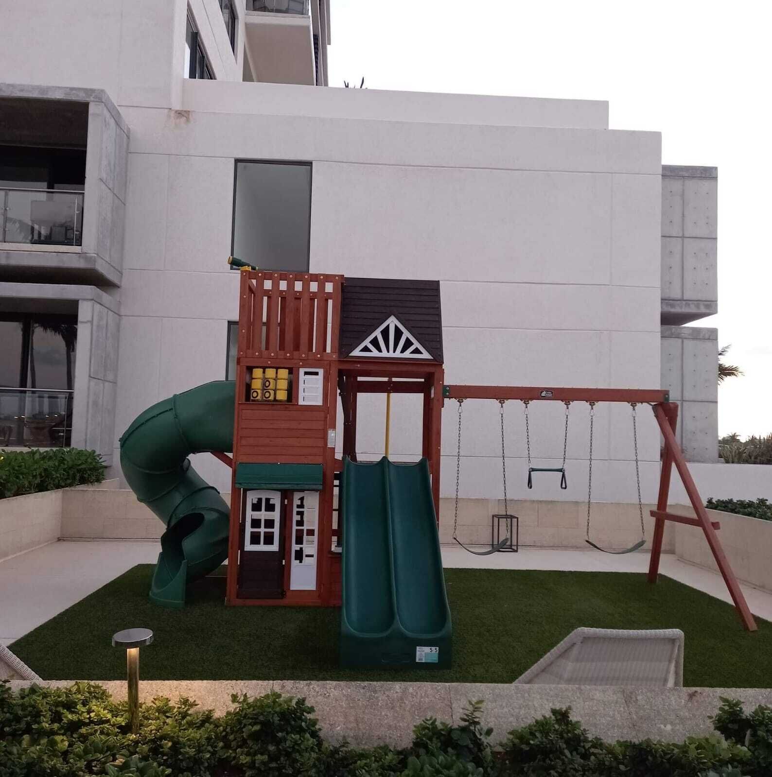 A playground with a slide and swings, set against a modern building facade.