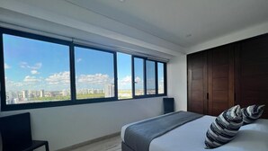 Ein Schlafzimmer mit großem Fenster, einem Bett, einem Sessel und Blick auf die Stadt.