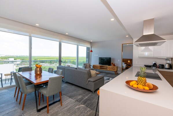 A modern living room with a large window, a dining area, and a kitchen. - Ocean view condo - Beach, pool & jacuzzi! (Cancún)
