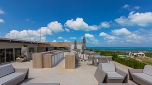 Eine Dachterrasse mit Außenmöbeln, einer Bar und Blick aufs Meer.