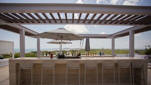 Ein Außenbereich mit Bar, der einen Meerblick bietet, mit einer Pergola überdacht und mit Barhocker und Sonnenschirmen ausgestattet.