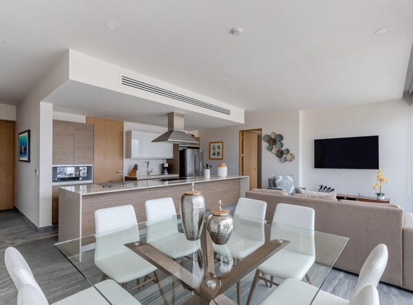 A modern living space with a dining area, kitchen, and a flat-screen TV mounted on the wall. - Exclusive apartment- Rooftop pool (Cancún)
