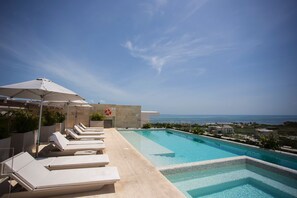 A rooftop pool with lounge chairs and umbrellas, overlooking a coastal view. - Exclusive apartment- Rooftop pool (Cancún)