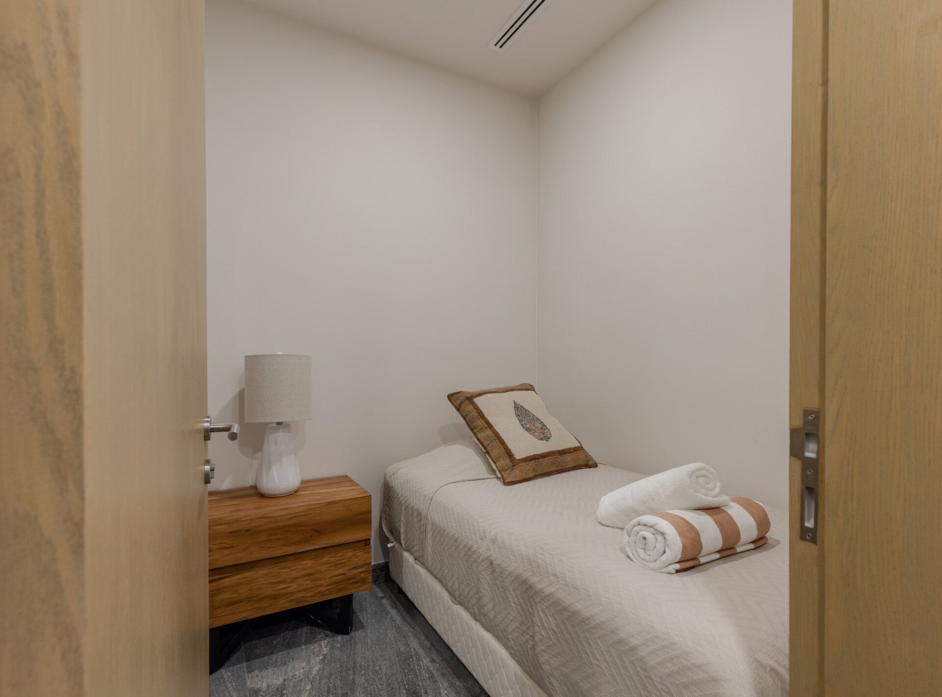 A small, neatly arranged bedroom with a bed, a bedside table with a lamp, and a wooden nightstand.