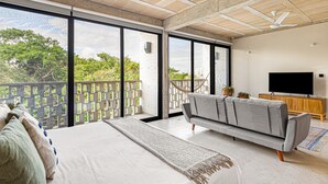 Ein geräumiges Zimmer mit einem großen Bett, einem grauen Sofa, einem Fernseher und einem Balkon mit Blick ins Grüne.