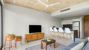 Ein modernes Wohnzimmer mit einer Couch, einem Couchtisch, einem Fernseher und einer Küchenzeile mit Barhocker.
