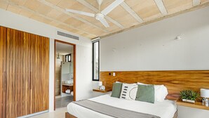Ein modernes Schlafzimmer mit einem Holz-Kopfteil, einem großen Bett, einem Nachttisch mit Lampe und Blick ins Badezimmer.