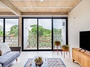 Relax in this stylish living room with a sofa, flat-screen TV, and hammock, leading to a balcony with potted plants.