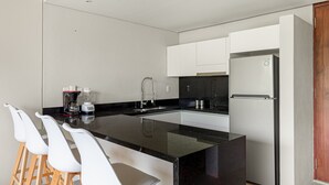 Eine moderne Küche mit schwarzem Arbeitsplatz, weißen Barhocker, einem Edelstahlkühlschrank und einer Kaffeemaschine.