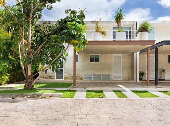A modern building with a stone facade, a covered outdoor area with potted plants, and a well-maintained lawn. - 4 bedroom house- private pool! (Cancún)