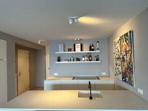 Una cocina moderna con armarios blancos, una isla central con un lavamanos y un estante empotrado con utensilios de cocina.