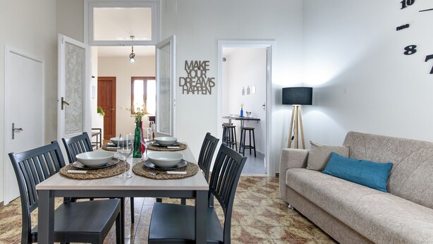 Un soggiorno moderno con zona pranzo, un divano e una cucina sullo sfondo.